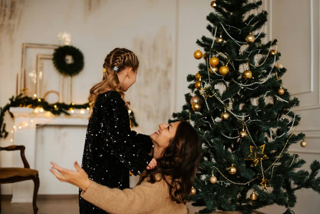 A mother and child sharing a joyful moment beside a Christmas tree in an unfamiliar holiday setting