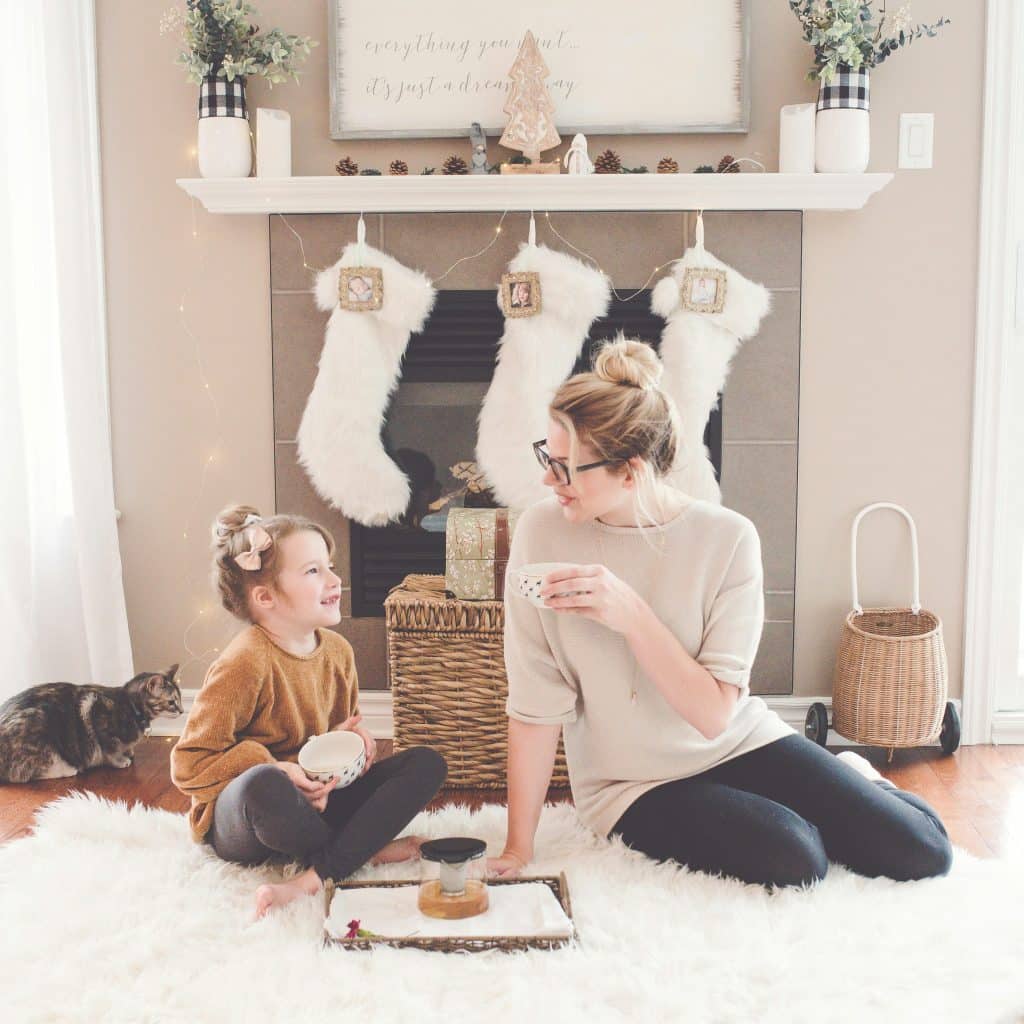 Modern mom and daughter sharing tea in a cozy holiday living room with stockings showing a calm and organized December supported by reliable childcare scaled