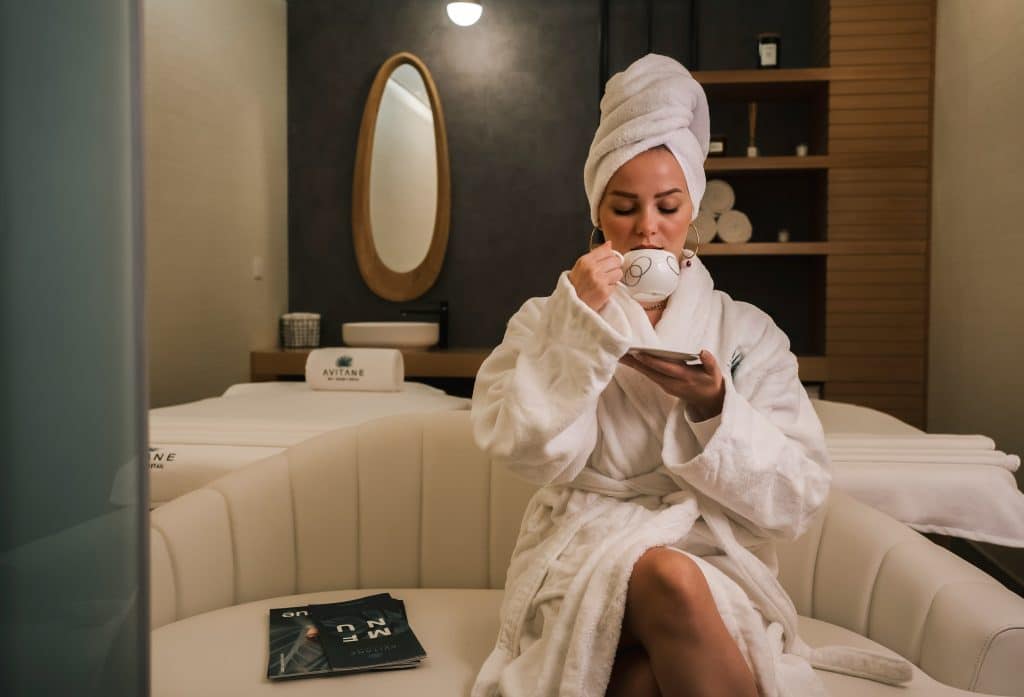 Woman in a hotel spa robe enjoying tea and downtime, representing the polished calm families can experience when childcare is seamlessly built into travel plans
