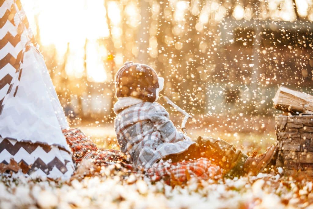 Young child bundled in winter clothes playing outdoors under soft falling snow at sunset, capturing a peaceful holiday moment that reflects the calm, supported December families can