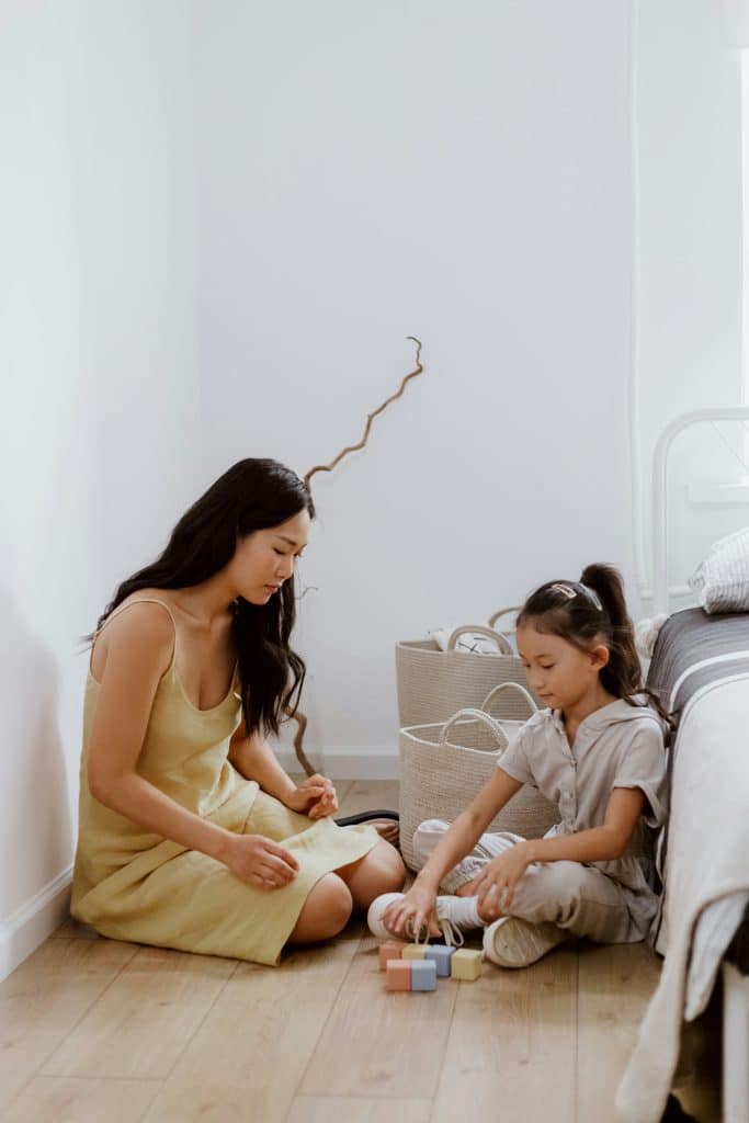 Adult and child sitting on the floor playing with wooden blocks in a calm, organized home environment