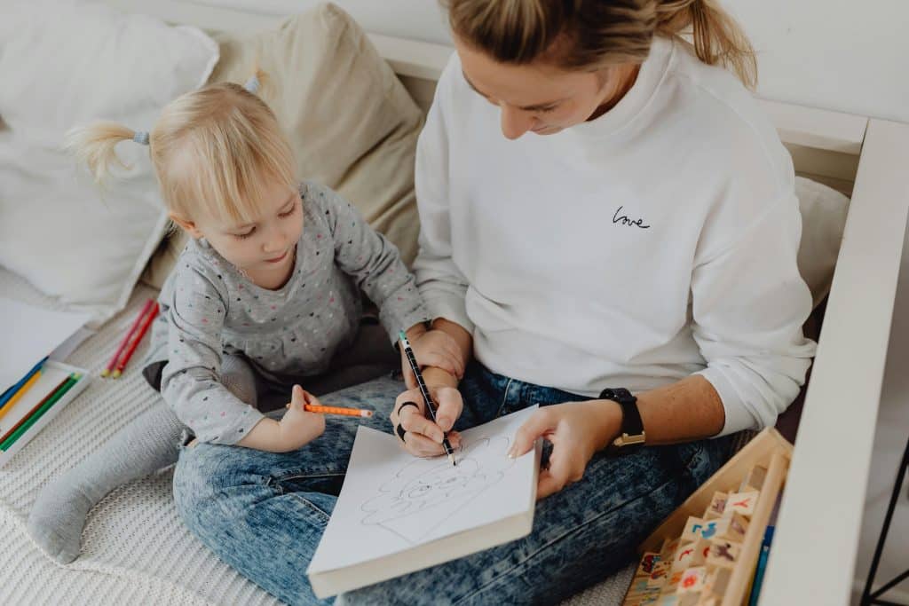 Adult and child sitting together on a bed drawing with colored pencils during a calm, unhurried moment at home