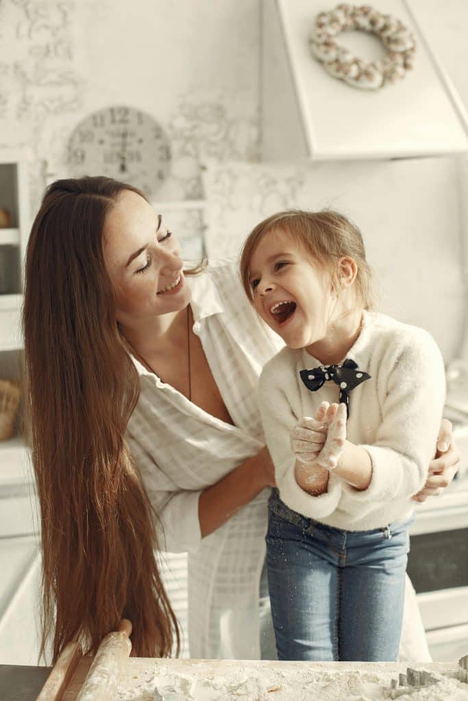 Adult and child standing together in a kitchen, smiling during a shared everyday activity in a calm home environment
