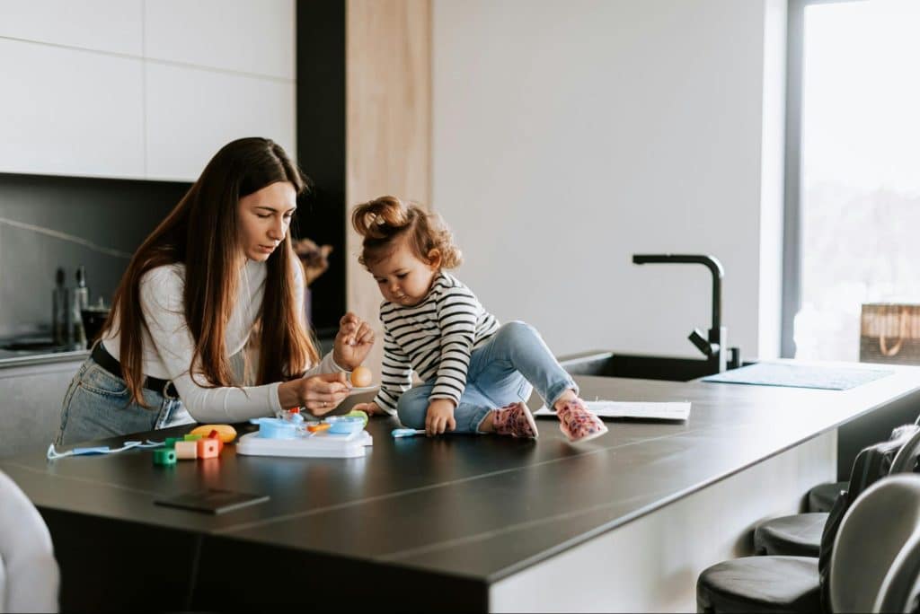 An adult and a toddler sitting at a kitchen island, interacting with toys in a modern home