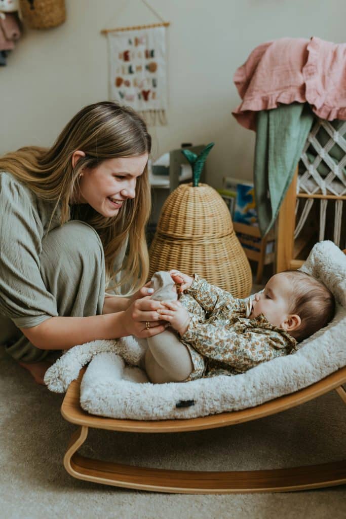Caregiver calmly engaging with an infant in a well organized home environment, illustrating how consistent support systems absorb daily changes without disruption