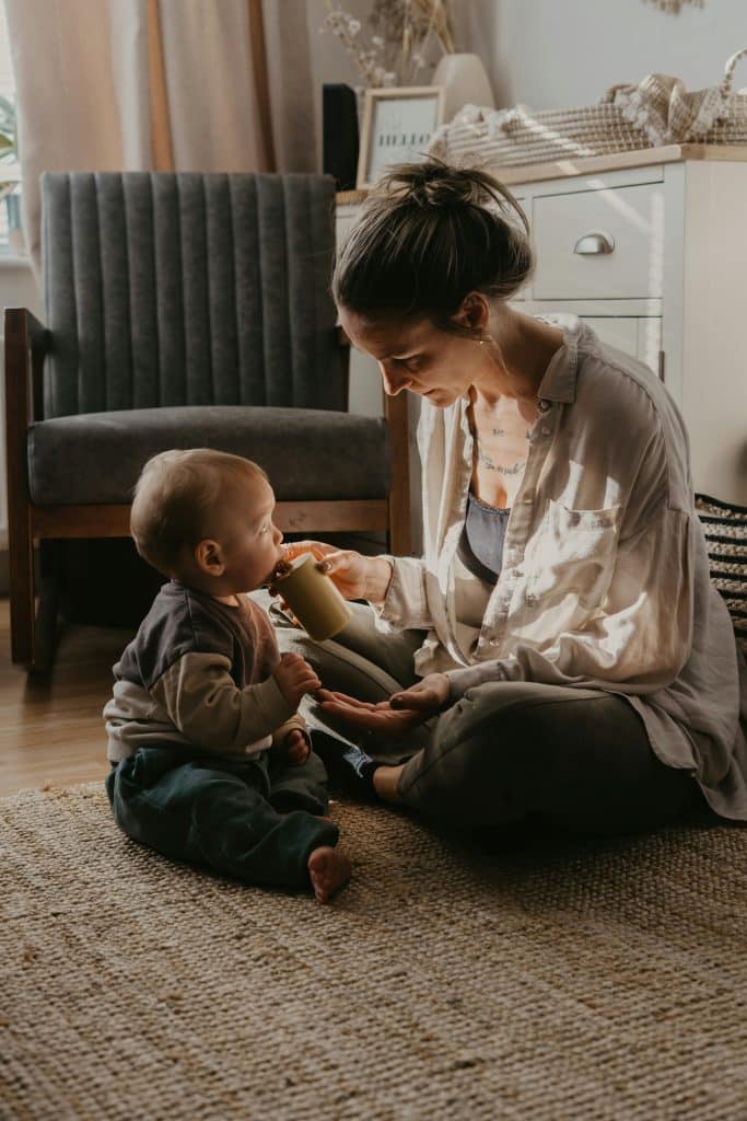 Caregiver calmly feeding a baby on the floor of a tidy living space, reflecting how stable routines reduce mental effort and constant decision making