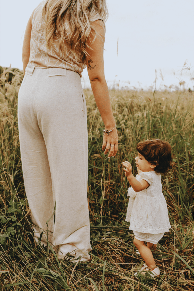 Mother walking through a field with her toddler, illustrating the quiet emotional labor and invisible responsibility of motherhood