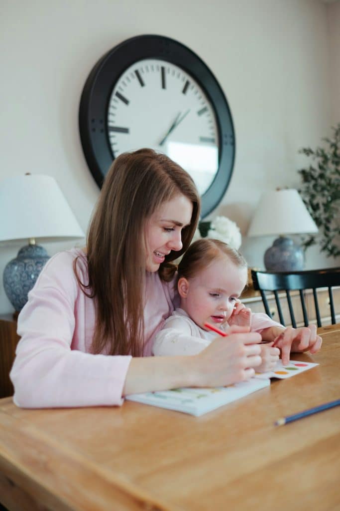 Caregiver helping a young child with drawing at the table during a calm afternoon at home