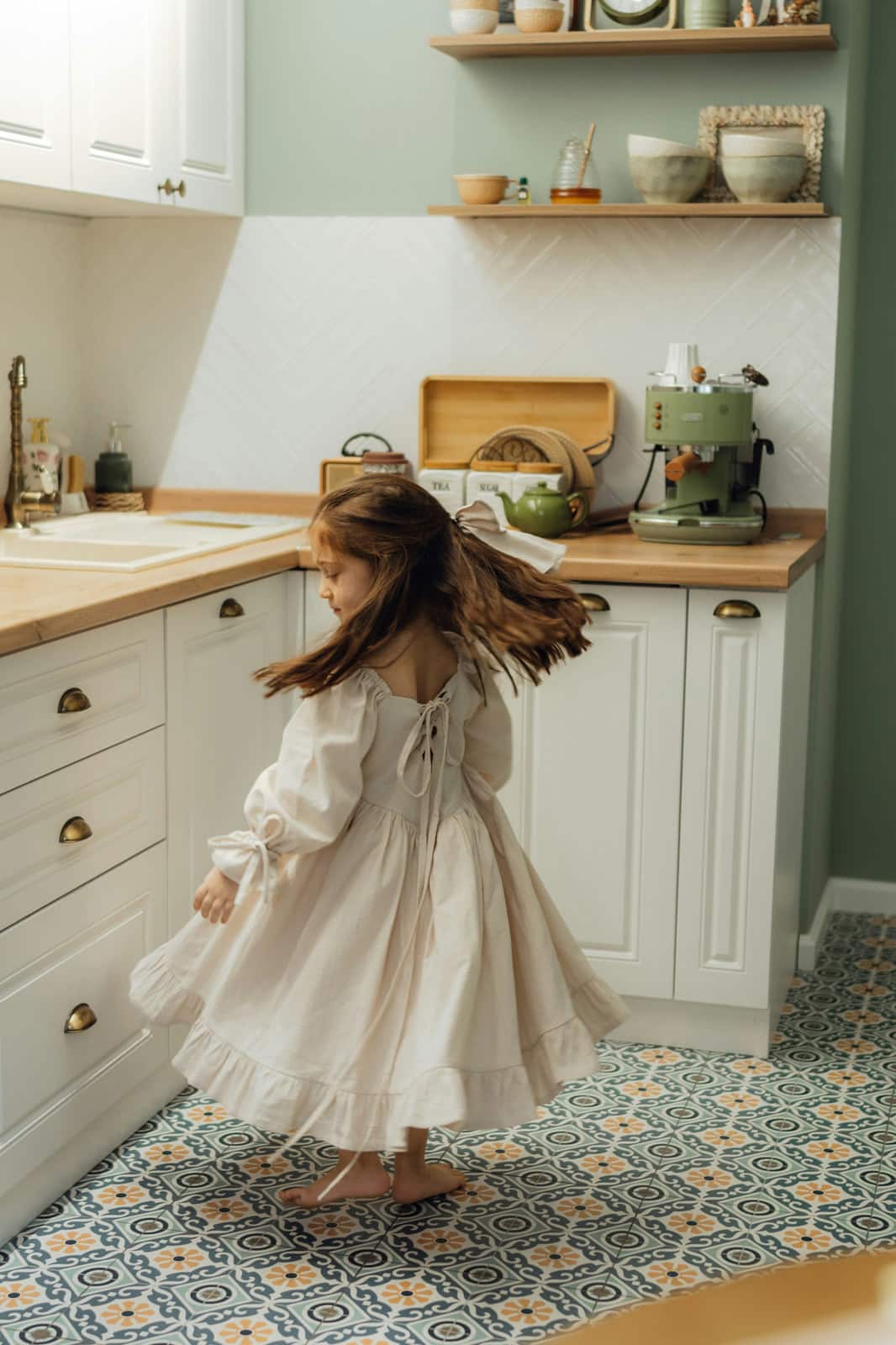 Young girl in a cream dress twirling in a sunny kitchen