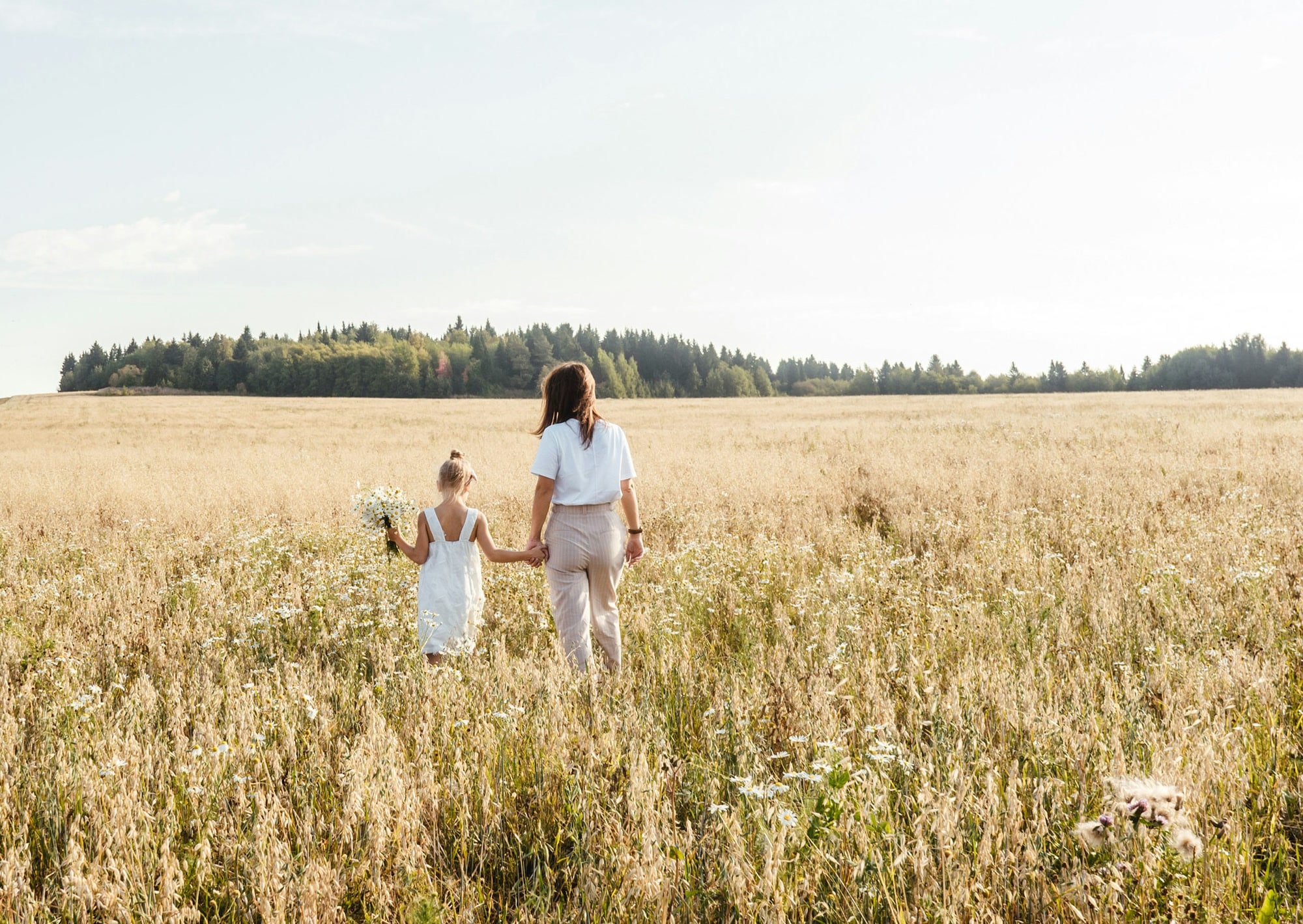 Mother and daughter walking hand in hand through a golden wildflower field