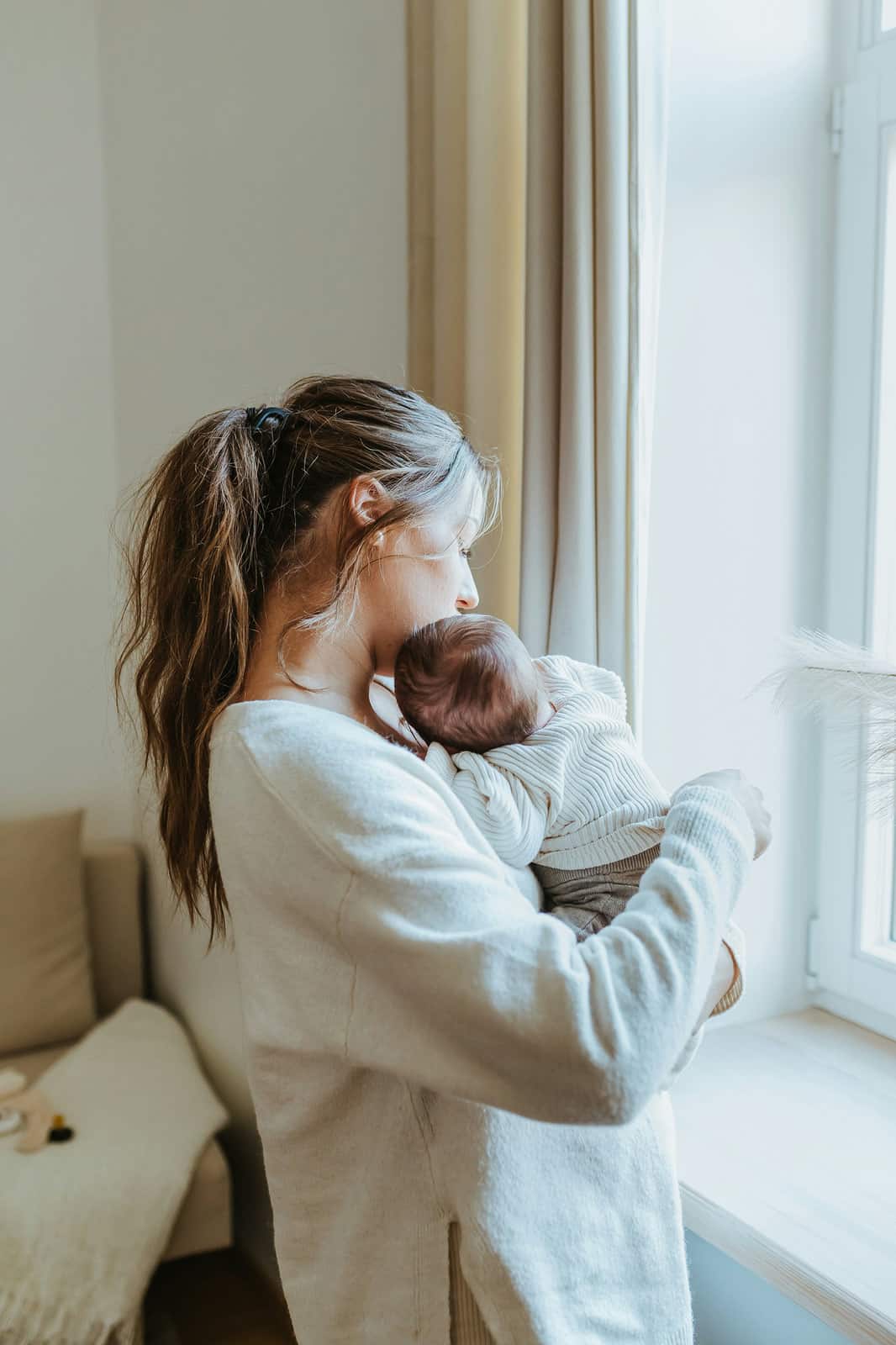 Mother holding her newborn baby close beside a bright window